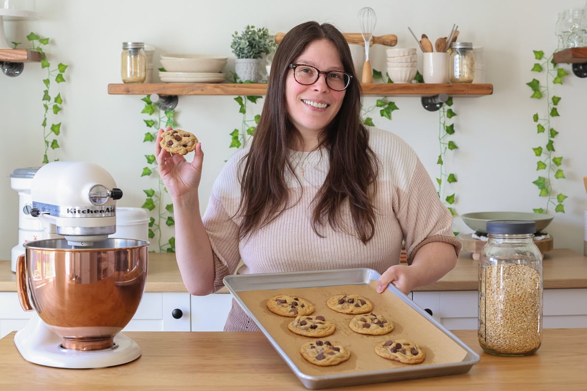 woman holding a cookie and a tray of cookies.