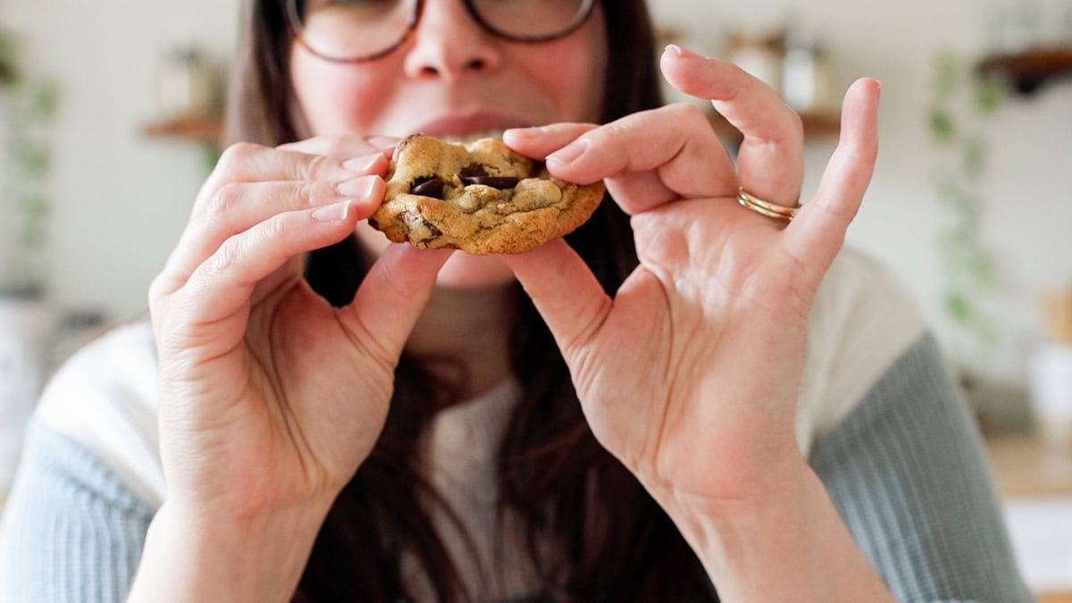 Woman holding a chocolate chip cookie with two hands.