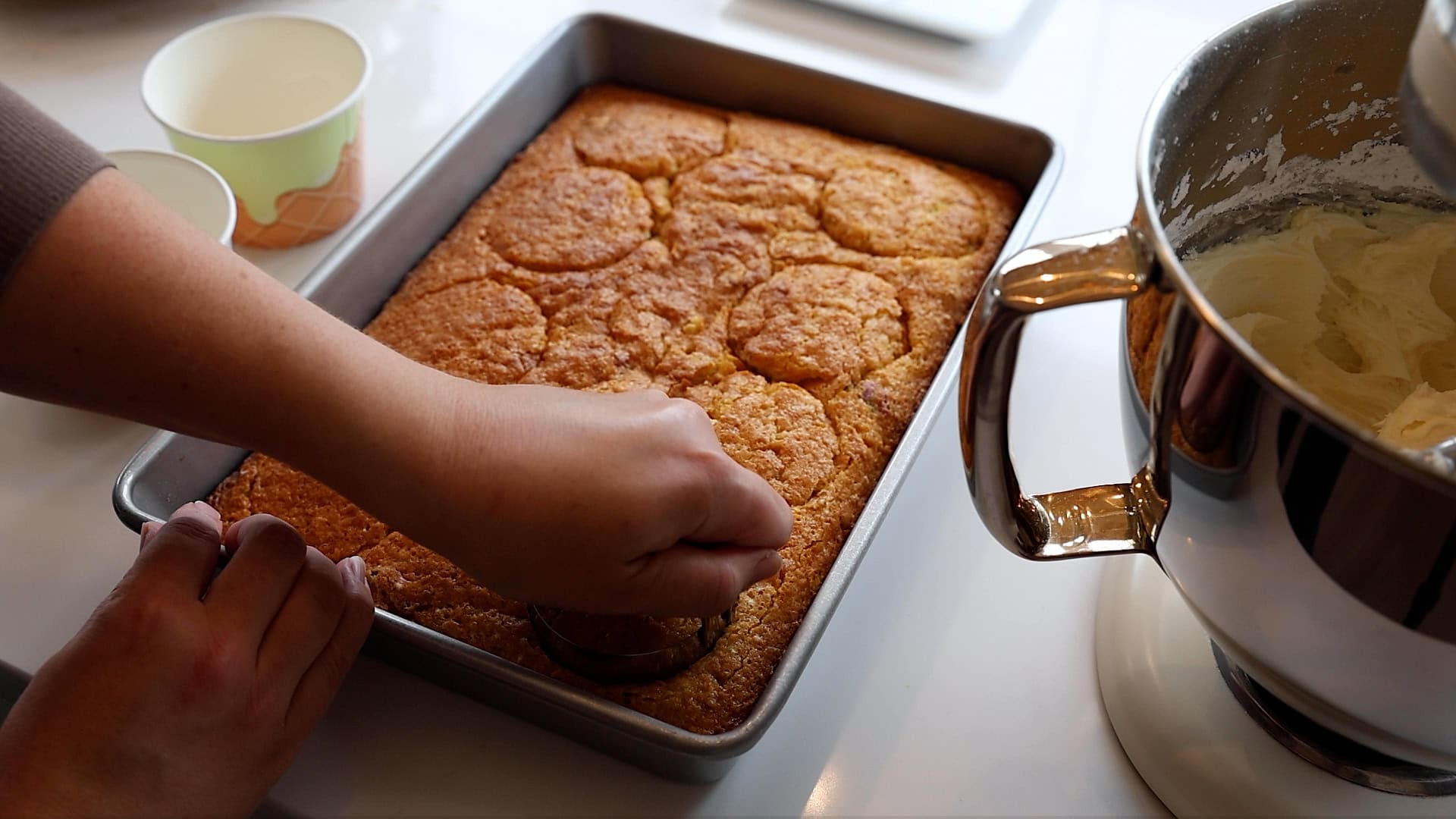 hand using biscuit cutter to cut out mini cakes in 9x13 cake pan.