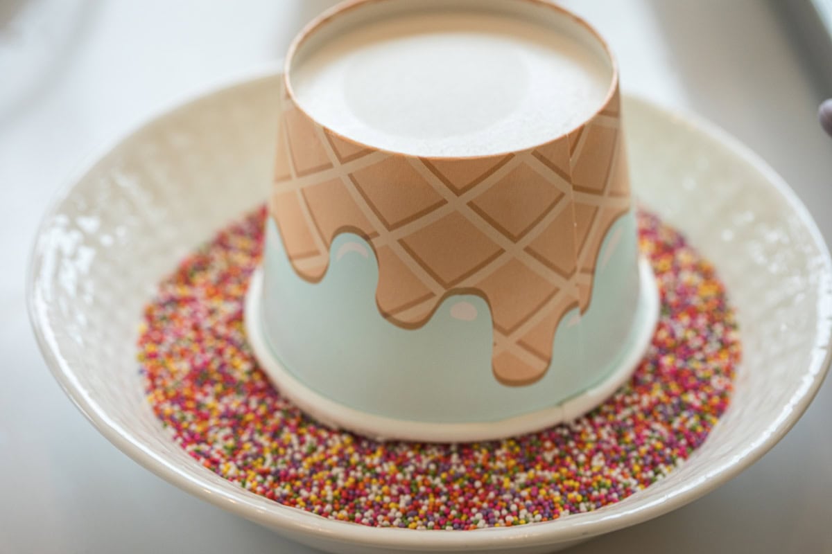 upside down snack cup filled with cake and buttercream in a bowl of nonpareils to make dot cakes.