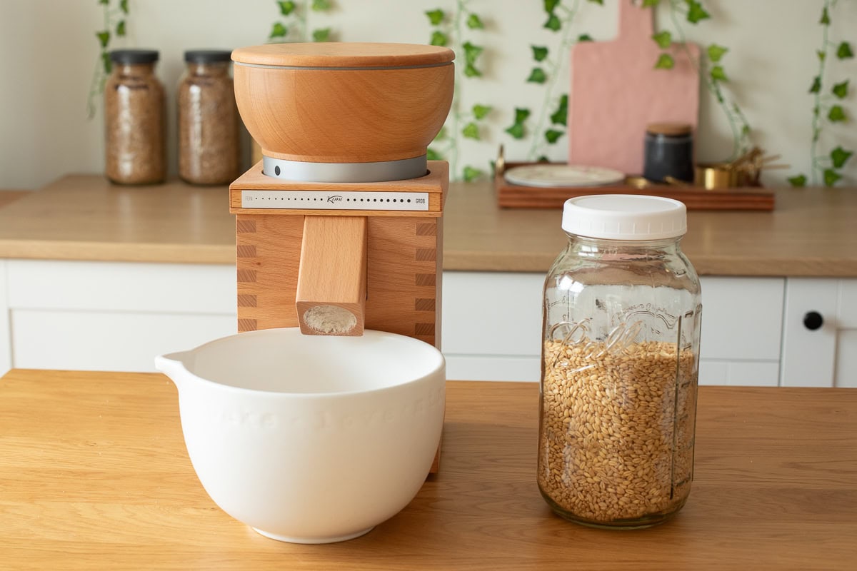white bowl and a komo vienna grain mill next to soft white wheat berries.
