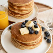 pancakes made with fresh milled flour on a white plate topped with a pat of butter, banana slices and blueberries.