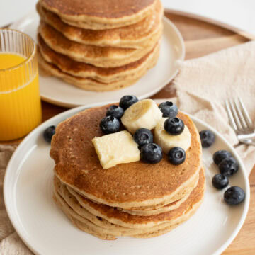 pancakes made with fresh milled flour on a white plate topped with a pat of butter, banana slices and blueberries.