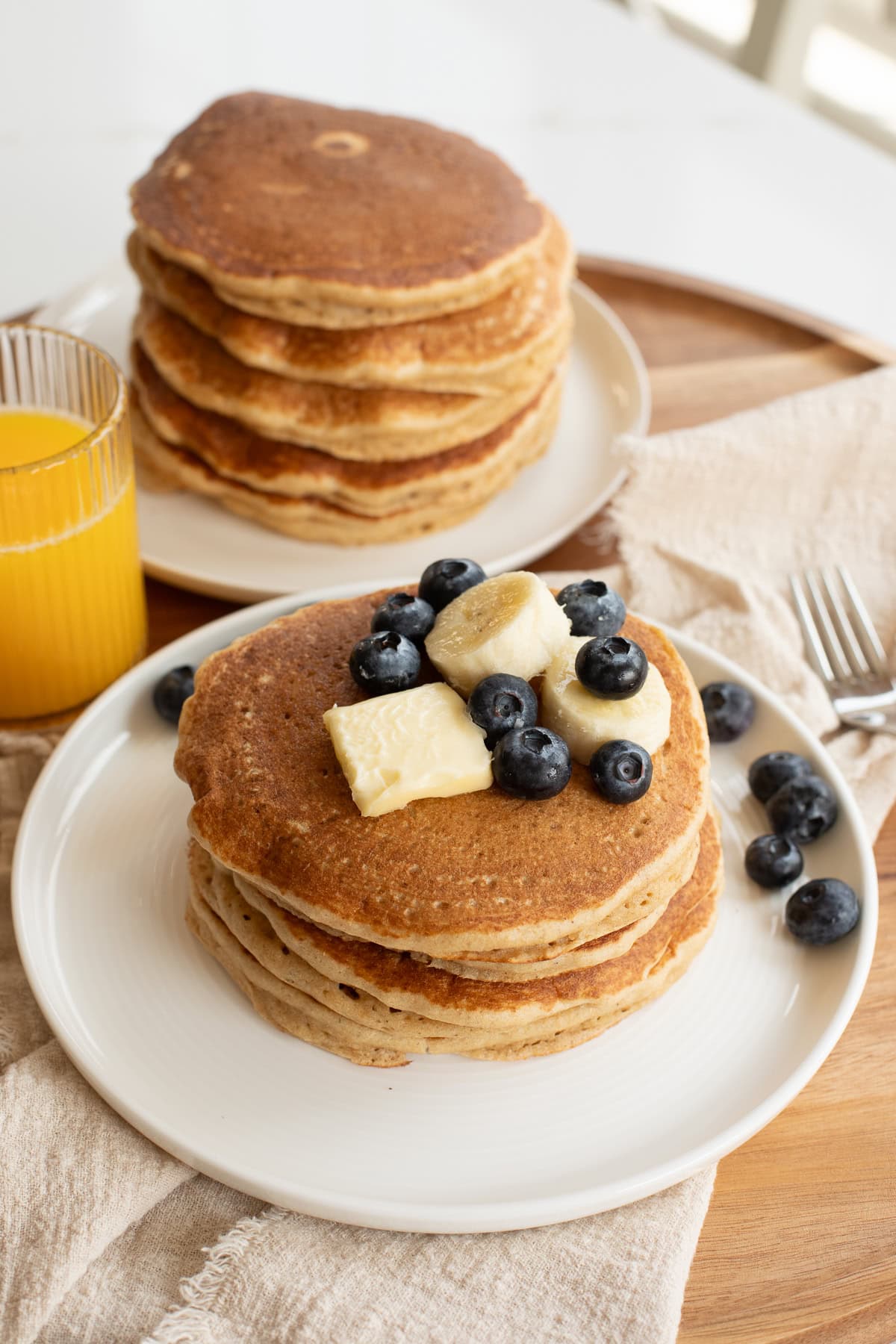 pancakes made with fresh milled flour on a white plate topped with a pat of butter, banana slices and blueberries.