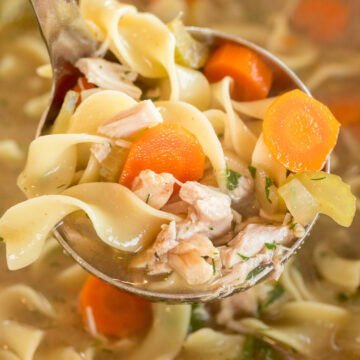 Slow cooker chicken noodle soup in a ladle with juicy chicken, vegetables, and tender egg noodles.