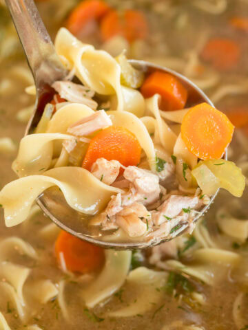 Slow cooker chicken noodle soup in a ladle with juicy chicken, vegetables, and tender egg noodles.