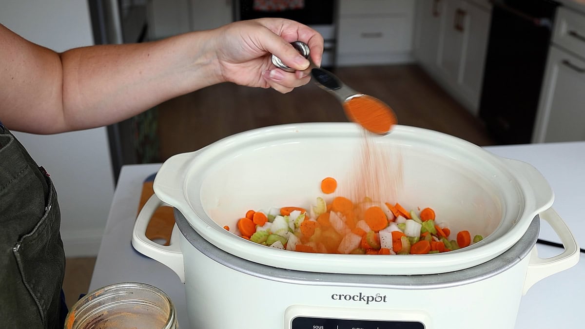 hand spooning in some tomato powder into crockpot.