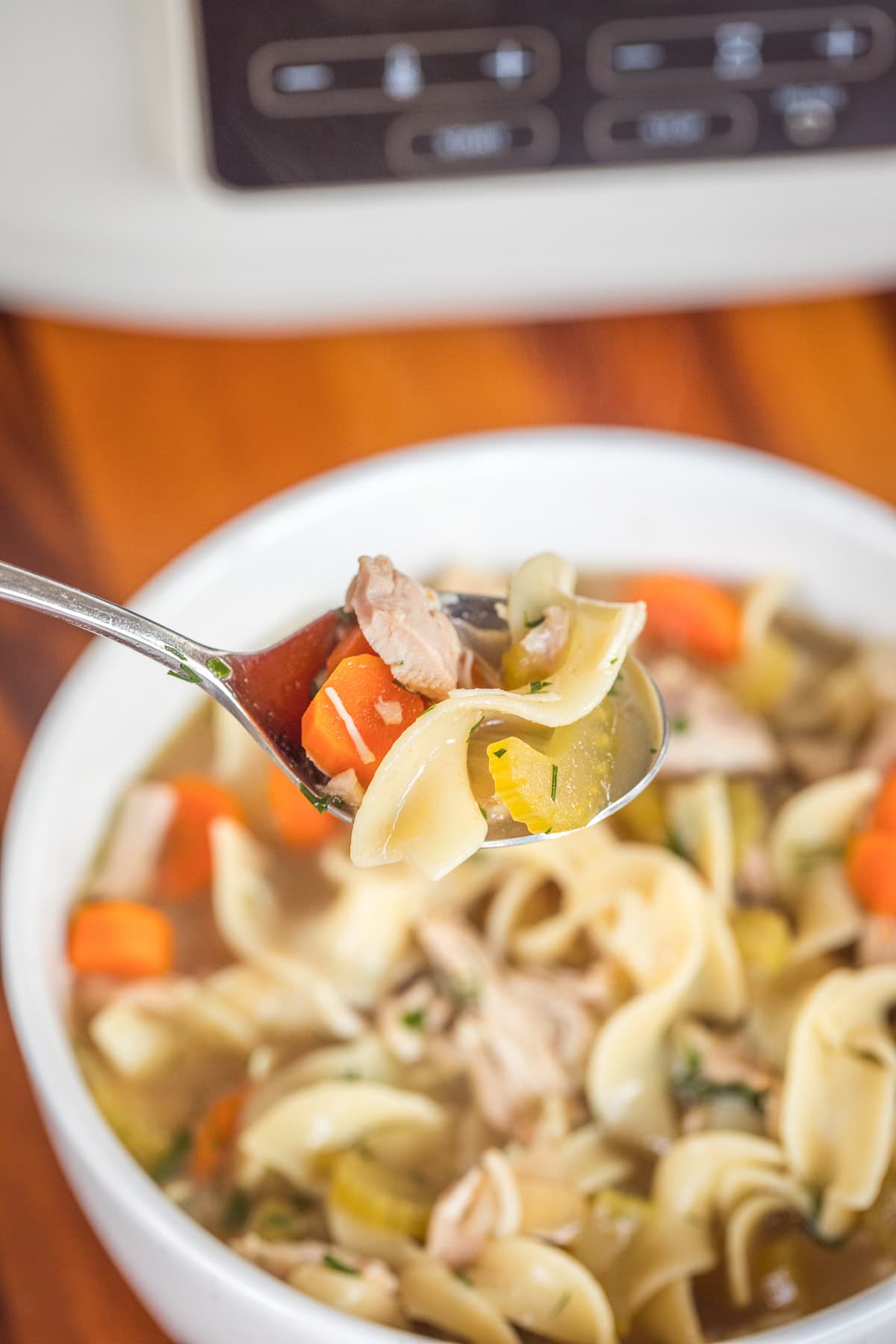Slow cooker chicken noodle soup in a white bowl with a spoonful being held up.