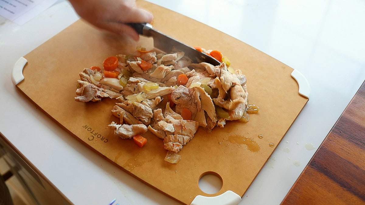 slow cooked chicken thighs being chopped on cutting board.