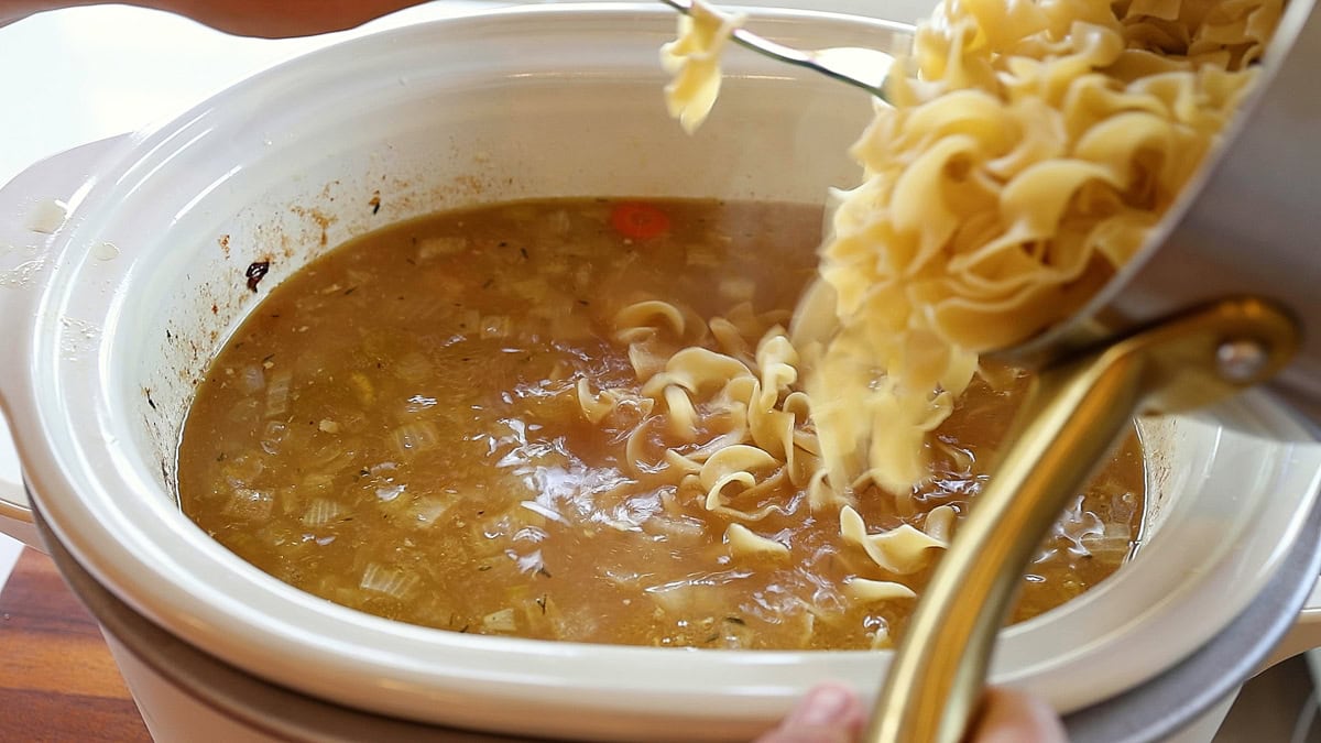chicken soup in crockpot with noodles being added.