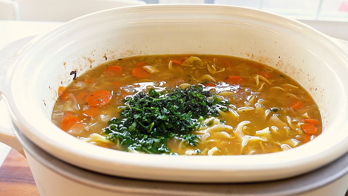slow cooker chicken noodle soup with herbs ready to be mixed in.