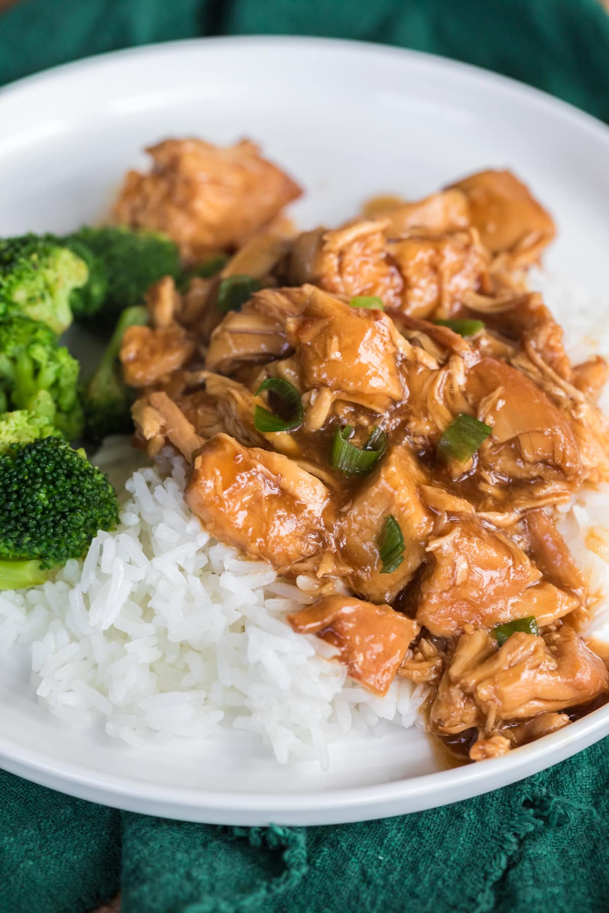 homemade slow cooker teriyaki chicken over rice with broccoli on a white plate.