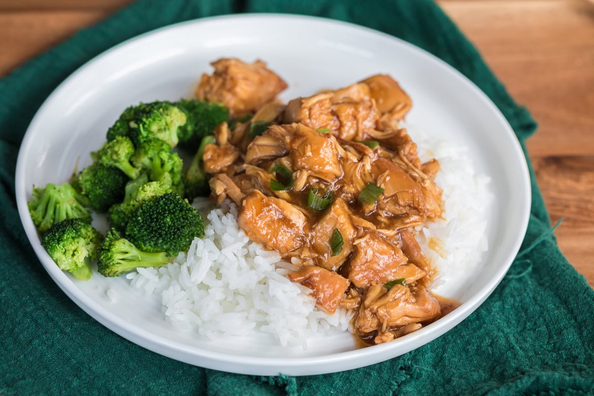 slow cooker chicken teriyaki over rice with broccoli on a white plate.