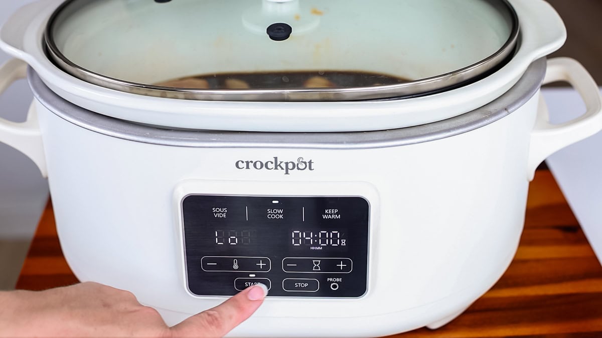 finger pushing buttons on a slow cooker.