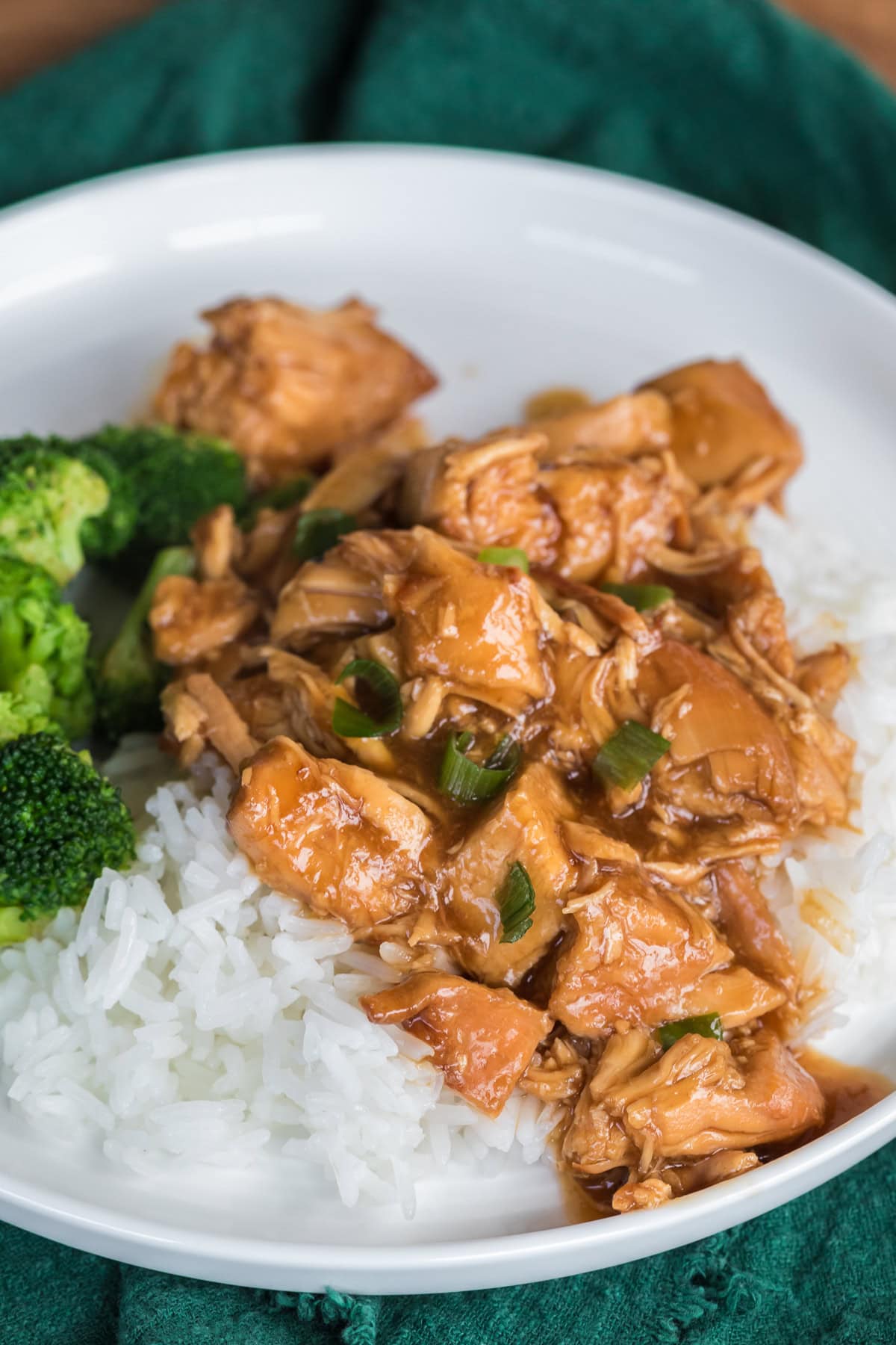 close up of slow cooker chicken teriyaki over rice with broccoli on a white plate.