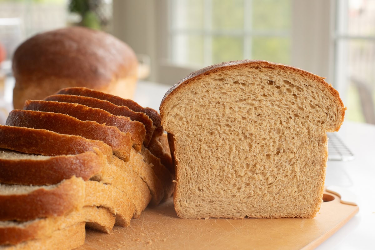 fresh milled flour bread on a cutting board showing half a loaf and slices.