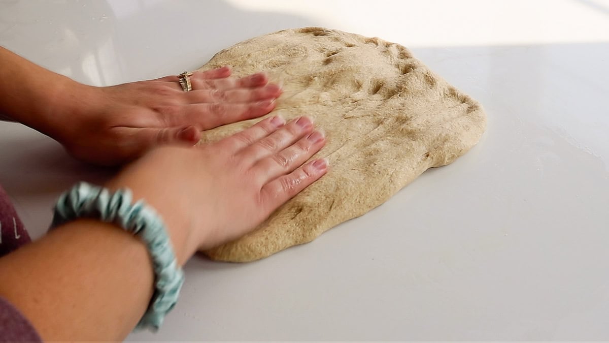 hands flattening fresh milled flour bread dough.