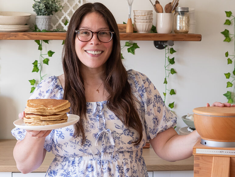 courtney of courtney's sweets holding a stack of fresh milled flour pancakes next to a komo mill in her studio.