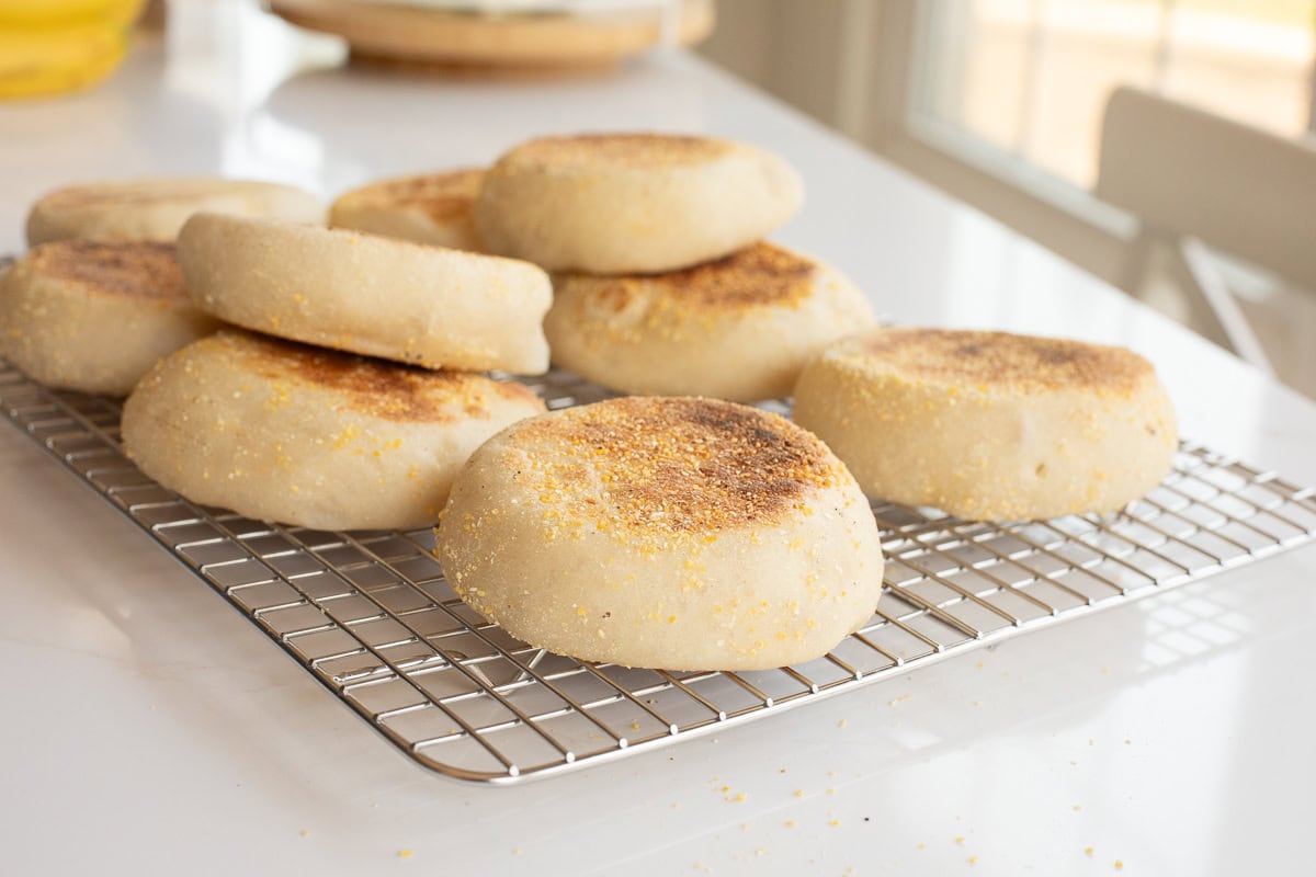 close up of a cooling rack on a counter with fresh english muffins on it.