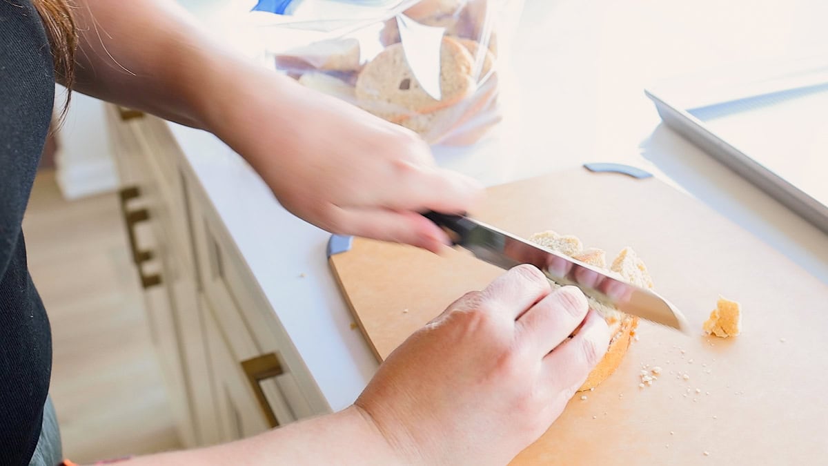 hands shown chopping up bread for bread crumbs on cutting board.