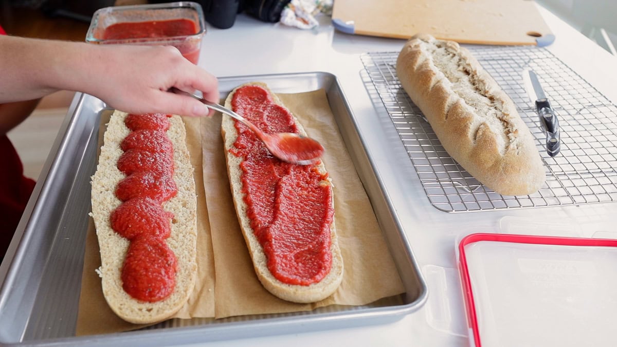 spreading pizza sauce onto french bread.