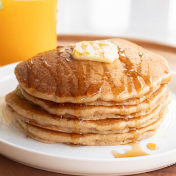 Stack of Einkorn pancakes with a pat of butter and a drizzle of maple syrup.