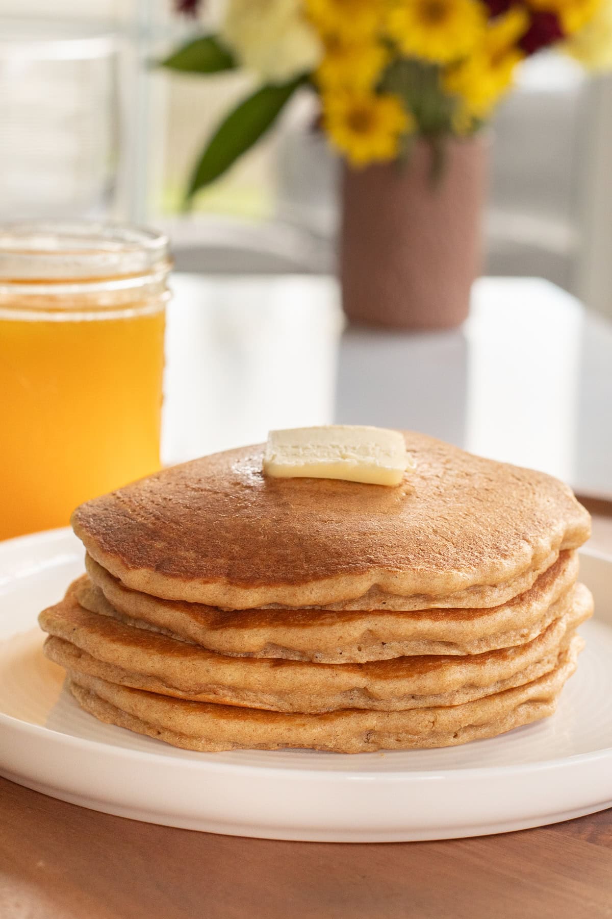 Fresh milled einkorn pancakes stacked on a plate with a pat of butter.
