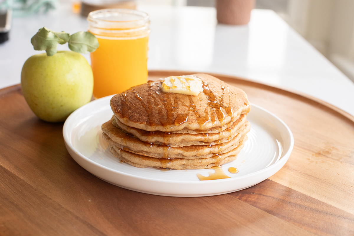 Stack of Einkorn pancakes with a pat of butter and a drizzle of maple syrup on top.
