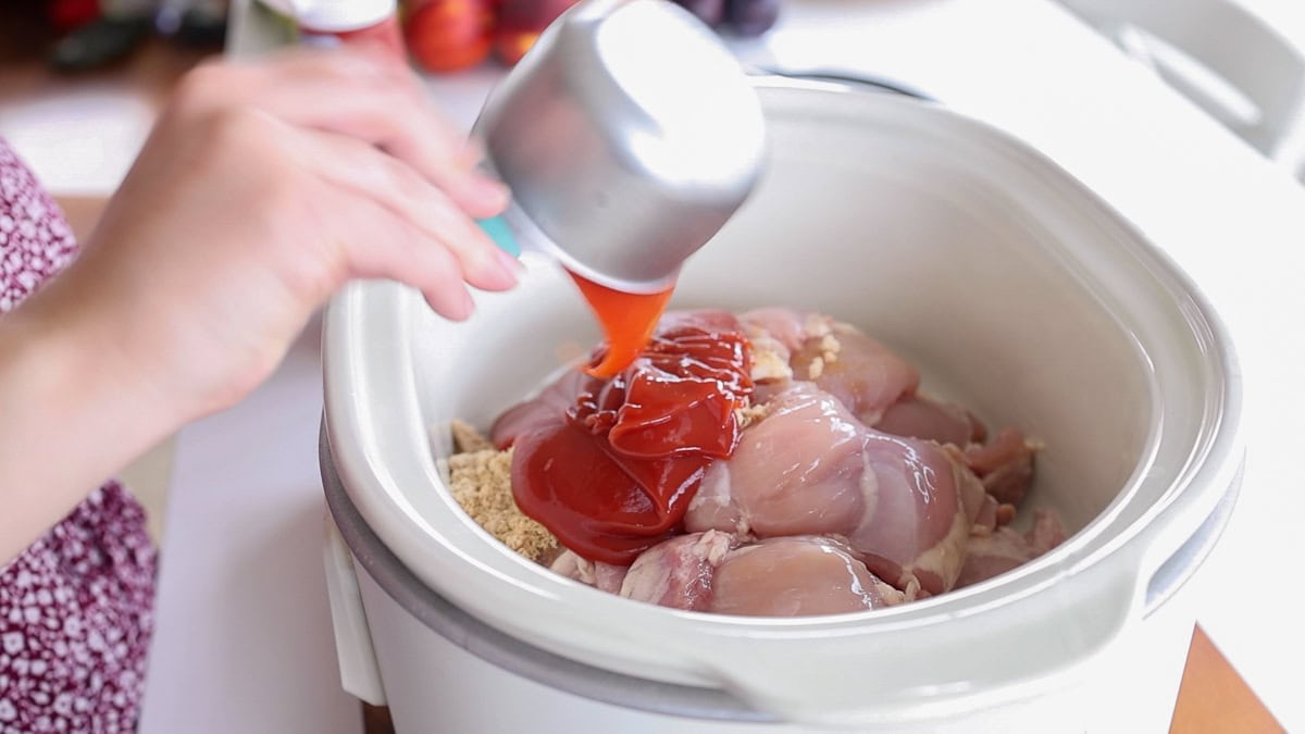 pouring ketchup over chicken thighs in slow cooker.