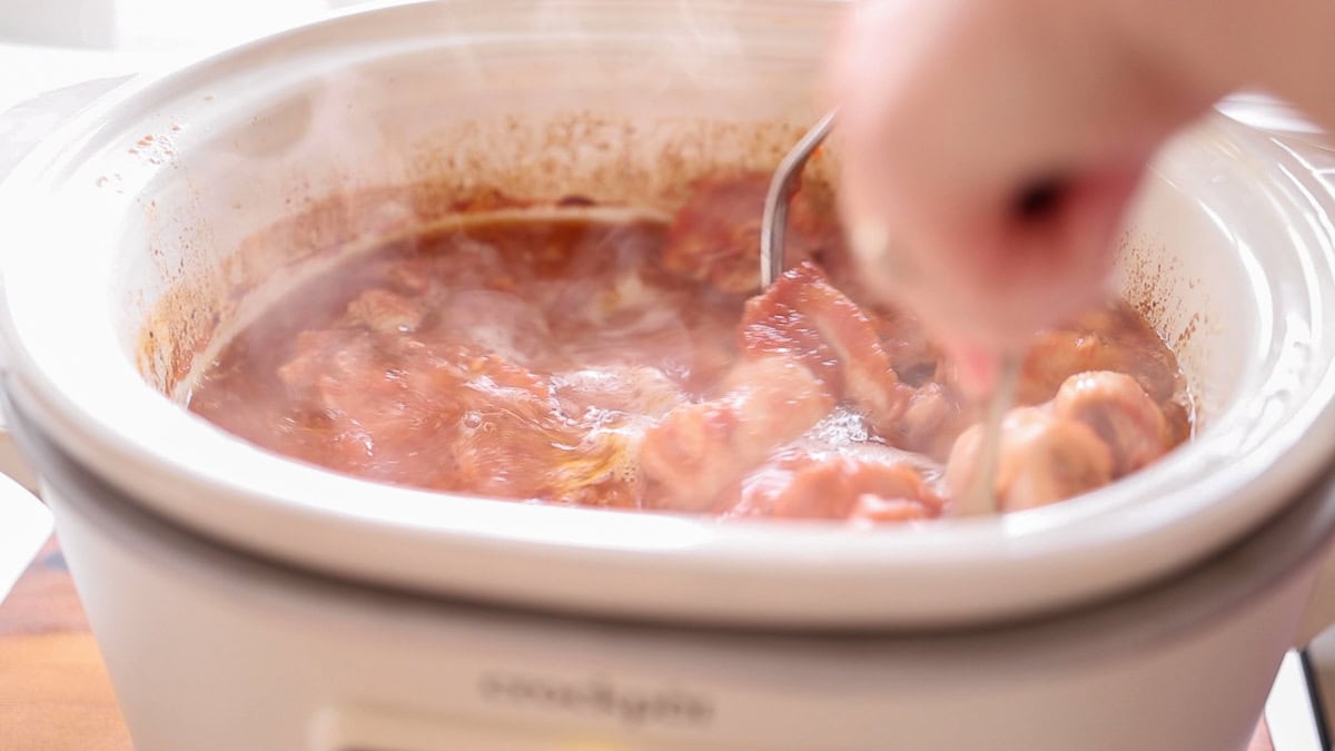 hands using forks to shred chicken thighs.