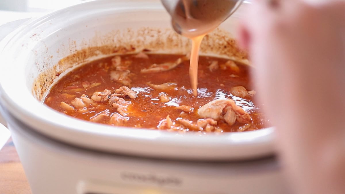 pouring cornstarch slurry into slow cooker chicken thighs.
