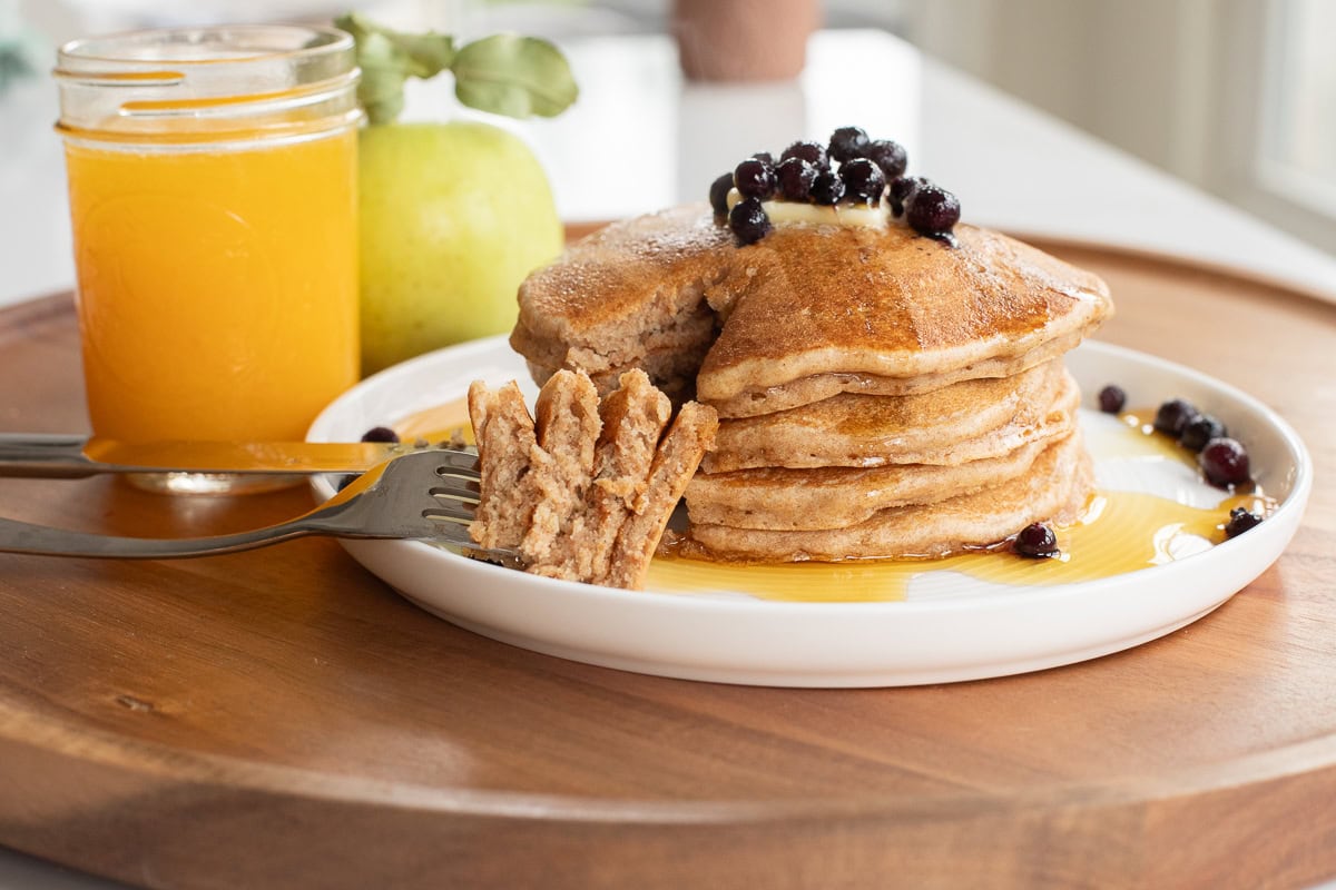 spelt pancakes stacked on a plate with a fork showing a bite amount to show texture of pancakes.