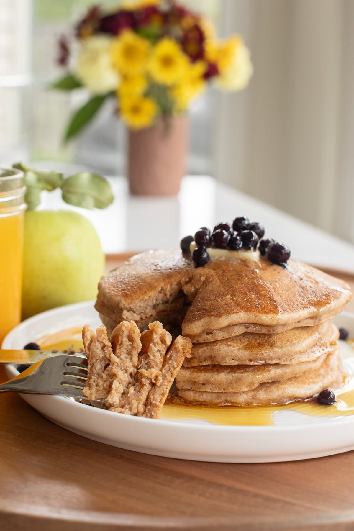 spelt pancakes stacked on a plate with a fork showing a bite amount to show texture.
