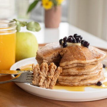 spelt pancakes stacked on a plate with a fork showing a bite amount to show texture.