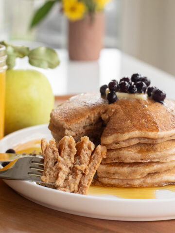 spelt pancakes stacked on a plate with a fork showing a bite amount to show texture.